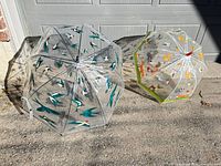 Both clear vinyl umbrellas opened; left shows teal swallow print, right shows woodland animals print with green trim