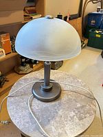 Full view of lamp showing brushed nickel base, stem, frosted glass shade, and power cord