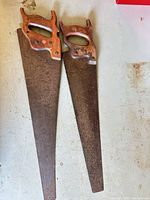 Two hand saws laid side by side showing full length, wooden handles, rusted blades