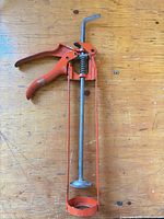 Full view of red-orange metal caulking gun lying on work surface
