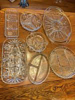 Group shot of seven pressed glass serving dishes on wooden surface showing variety of shapes and patterns