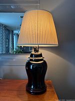 Full view of lamp on table showing shade, ceramic body and wooden base