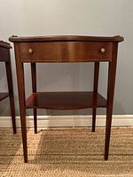 Front view of mahogany end table showing drawer, lower shelf, tapered legs