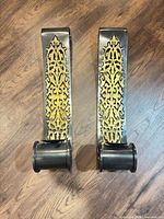 Front view of both black metal wall sconces displaying brass fretwork