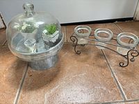 Glass cloche with faux plants and tealight cup next to metal votive holder