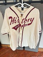 Front view of cream baseball jersey with burgundy History Television logo and trim