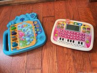 Front view showing both learning toys: Blue LeapFrog interactive book and pink/white VTech keyboard tablet
