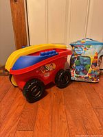 Red, blue and yellow pull-along wagon beside blue Mega Bloks bag