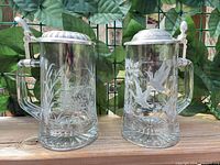 Front view of both etched glass beer steins with pewter lids