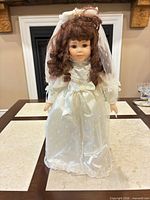 Full view of porcelain bridal doll standing on table wearing ivory dress and veil