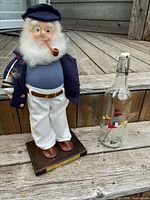 Full view of sailor doll beside glass bottle