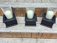 Three black wood/MDF bases each with crackle glass hurricane and ivory candle displayed on steps