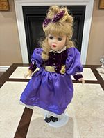 Front view of porcelain doll on stand showing attire and overall condition