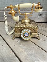 Front view showing ornate brass body, ivory handset, rotary dial, coiled cord