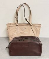 Front view of Coach ivory tote behind brown toiletry bag