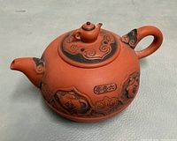 Left profile of reddish-brown clay teapot showing relief decoration and spout