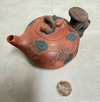 Side and top view of teapot beside coin for scale
