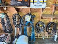 Multiple coiled extension cords, hose and cable reel hanging on wall