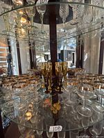 Display cabinet shelf showing multiple gold-rimmed coupe glasses, gold flutes and cordial goblets