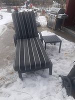 Chaise lounge with striped cushion and side table on snow-covered patio
