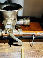 overall view meat grinder clamped to shelf with handle and funnels visible