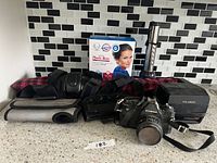 Group shot showing all items: Cosina SLR, Polaroid 660, boxed Magic Bag, red plaid compress, flashlight, braces/wraps