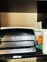 FoodSaver V3230 vacuum sealer on shelf with bag roll box and loose roll