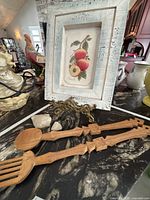 Framed peach still life, brass easel, carved salad servers displayed on countertop
