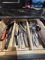 Drawer showing mixed stainless steel utensils and knives in three sections