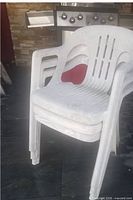 Stacked white plastic patio chairs in front of barbecue