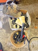 Top view of box and basket containing various black PVC parts, cream fittings, rubber couplers, and corrugated hose