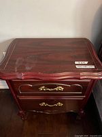 Front and top view of mahogany veneer nightstand showing two drawers, brass-tone handles, curved edges and carved legs