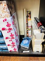 Shelf with stacked tissue boxes, foil and wrap rolls, foam containers and Kleenex pocket pack