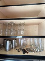 Cabinet shelves with wine glasses, stainless mugs, glass mugs, highball glasses, bar tools
