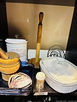 Group shot showing all items on shelf: canister, paper towel holder, mortar set, napkin holder, casserole with lid, blue baking dish, toothpick jar, seashells