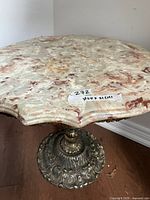 angled view of marble top showing scalloped edge and veining, label with dimensions visible, partial view of ornate base