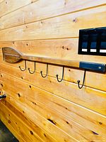 Full view of wooden oar coat rack mounted on wood wall showing six hooks and black accent plate
