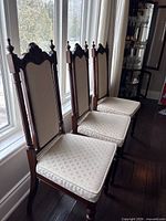 Three matching carved wood dining chairs lined at window