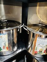 Both stainless steel stock pots with lids on shelving