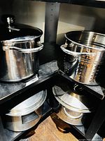 Four stainless stock pots of various sizes, three with lids and one perforated insert