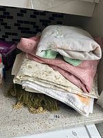 Stack of folded linens showing embroidery, damask and floral patterns, plus green fringe