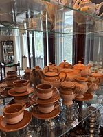 Full tea set on glass shelf showing cups, saucers, teapots, creamer and sugar bowl