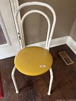Full view of vintage metal chair showing white tubular frame, yellow round metal seat, paint chips