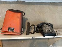Overview of orange metal case, cast flat iron, black rotary telephone on shelf