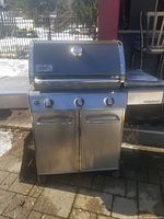 Front view of Weber Genesis grill showing three knobs, cabinet doors, side shelves, lid with thermometer