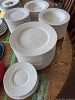 Stacks of white dinner and salad plates with basketweave rims on table