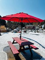 Full view of picnic table with benches and red umbrella set up outdoors on patio