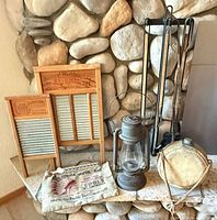 Group shot of both washboards, lantern, water bag, canteen, fireplace tools against stone backdrop