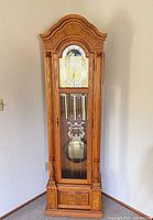 Front view of full grandfather clock showing oak case, arched bonnet, dial and lower cabinet