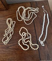 All four faux pearl necklaces laid out on wood surface